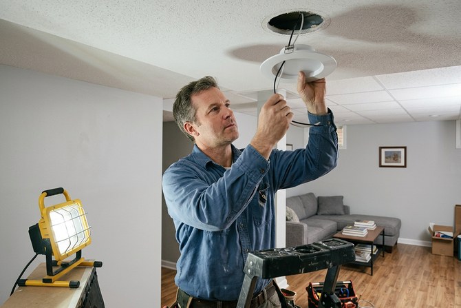 Electrician installing a new recessed light in a finished basement ceiling